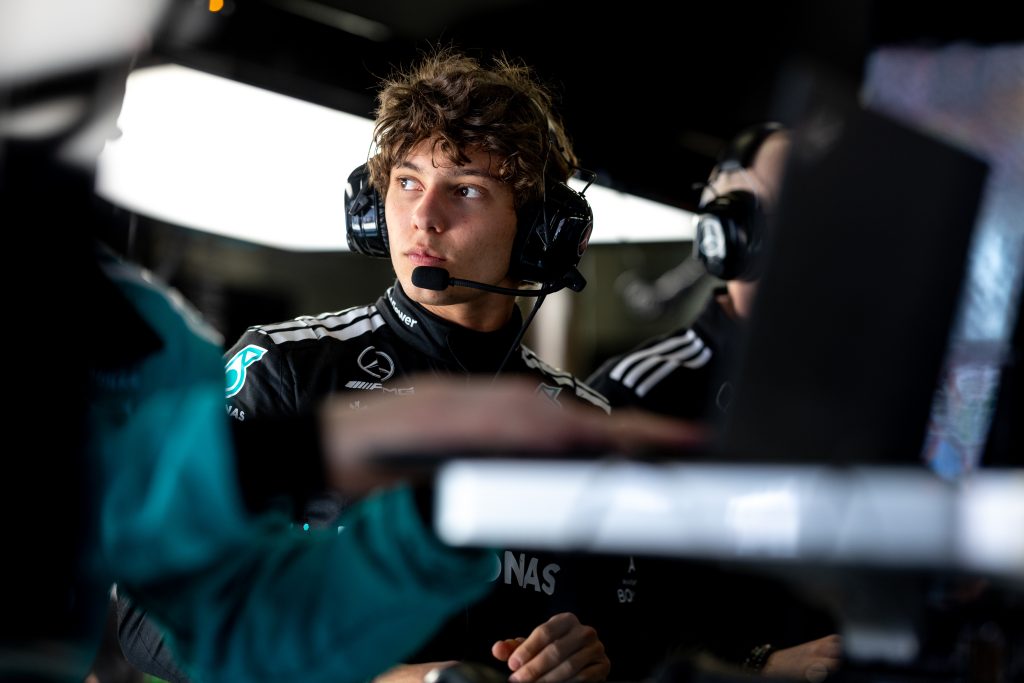 Andrea Kimi Antonelli, wearing a Mercedes team race suit and headset, focuses intently while working in the garage during a Formula 1 event.