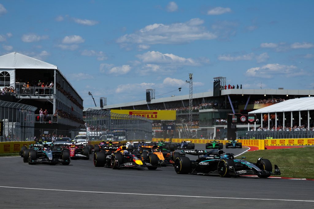 George Russell’s Mercedes (silver with black elements and turquoise accents) #63 leads the field into the corner, with Max Verstappen’s Red Bull (dark blue with red and yellow details) #1 chasing behind, while Andrea Kimi Antonelli’s Mercedes (si...