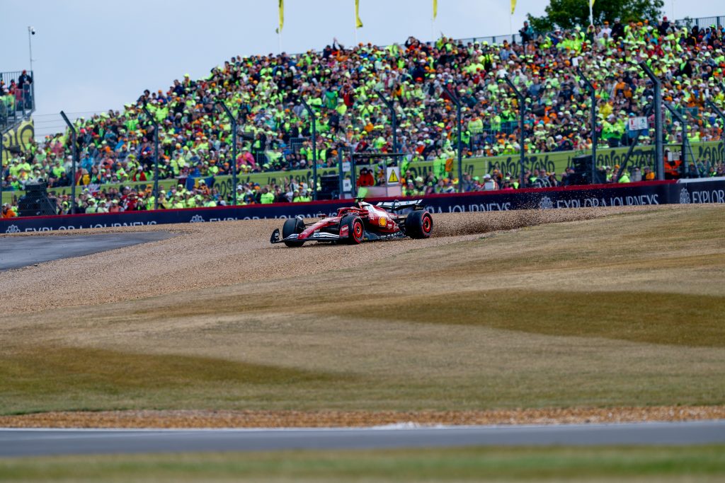 Charles Leclerc’s Ferrari (red car), #16, runs wide through the Silverstone gravel trap, spraying stones as he tries to recover back toward the circuit.