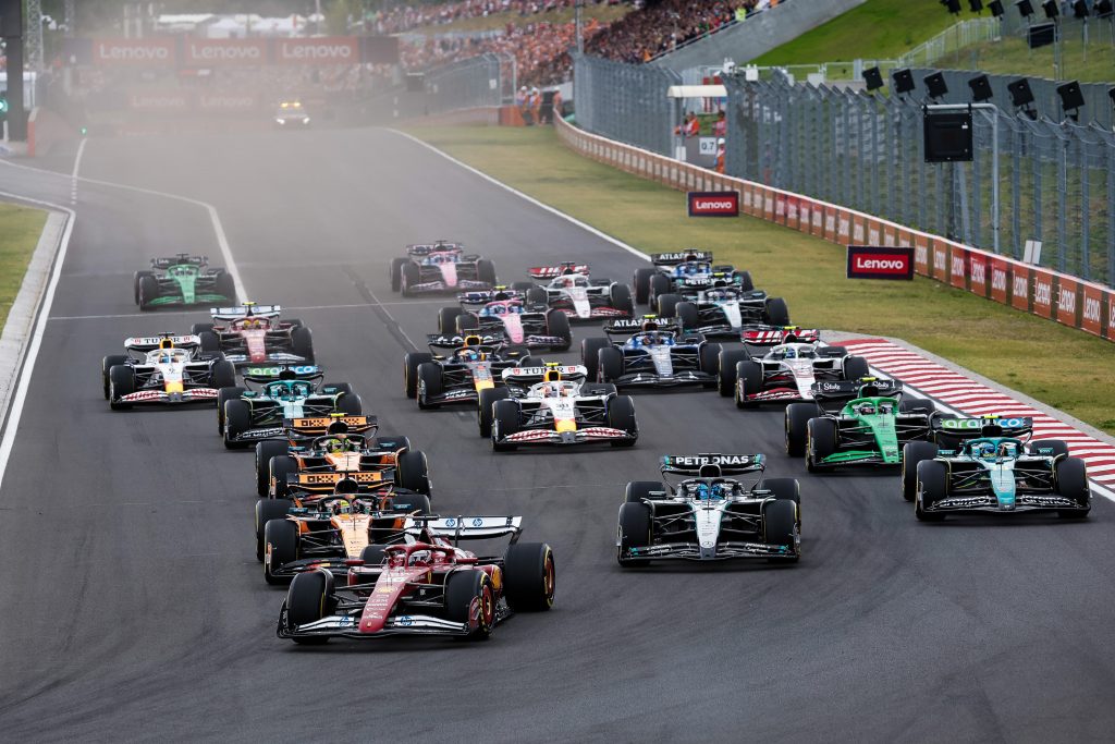 Leclerc’s Ferrari (red car) #16 leads the charge at the start, with two McLaren (orange cars) — Norris #4 and Piastri #81 — tucked in just behind, while Russell’s Mercedes (silver car) #63 runs to the right and Alonso’s Aston Martin (green ca...