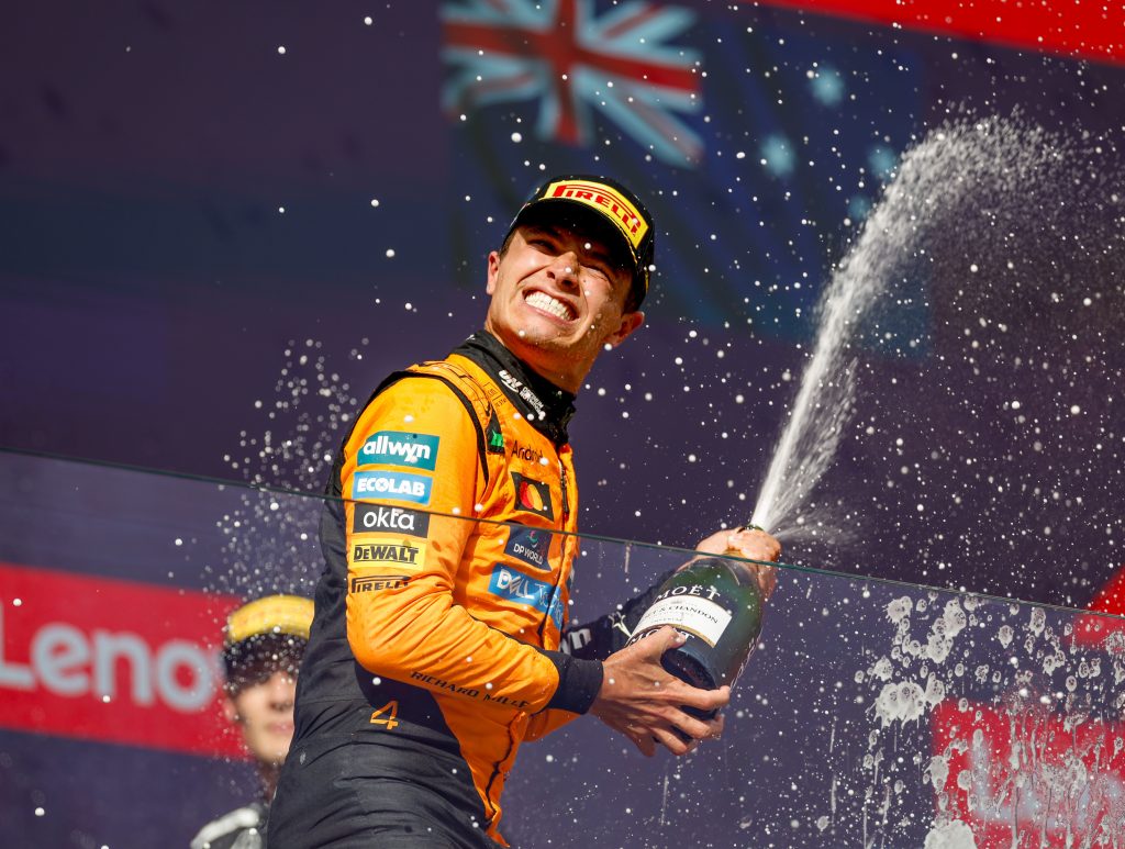 McLaren driver Lando Norris celebrates on the podium, spraying champagne.