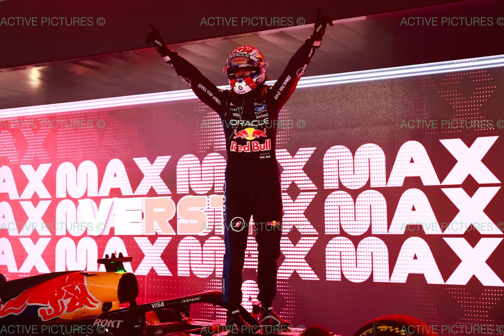 Red Bull driver Max Verstappen stands atop his car with both arms raised in celebration.